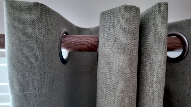 Close-up view of grey grommet curtain fabric hung on a wooden rod with metal eyelets, showing texture.