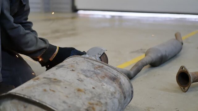 Auto mechanic uses electric cutoff grinder to cut part of car muffler. Mechanic cuts resonator from exhaust for repair. Welding and repair work in auto service.