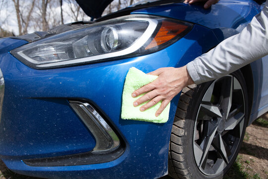 Man cleaning a blue car with a microfiber cloth and a rag