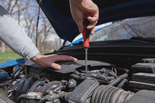 Close-up of a man's hand with a screwdriver repairing a car