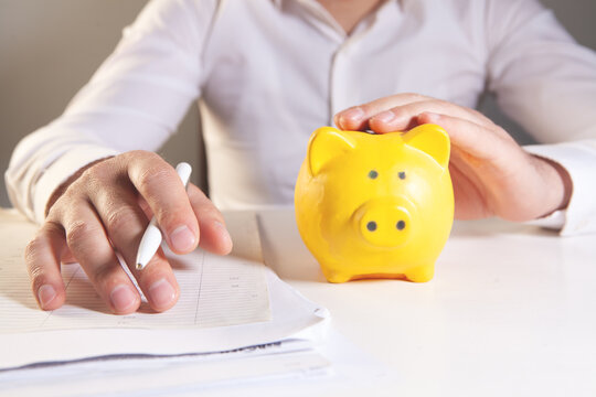 Businessman putting coin into piggy bank and writing on notepad