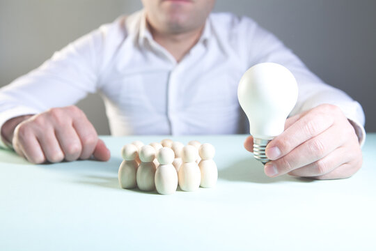 Businessman with light bulb and wooden figures on the table. Business concept.
