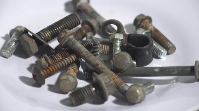 Close up of a rotating pile of various old rusty metal bolts, screws, and nuts on a white plate, showing heavy industrial texture.