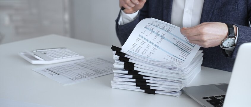 Auditor or accountant inspecting financial documents with a magnifying glass. Analyzing corporate tax records. Legal data. Invoice details. Or business reports. Audit and taxes
