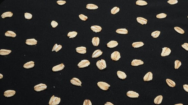 Macro of organic rolled oat grains scattered on black background rotating, food texture.