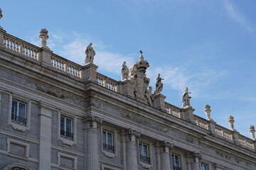 Fototapeta premium Rooftop Statues and Royal Coat of Arms on Palacio Real Facade Against Blue Sky Madrid