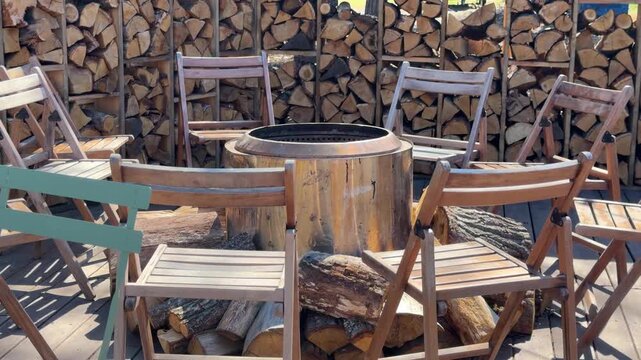 Wooden chairs around fire pit with wood stacked background