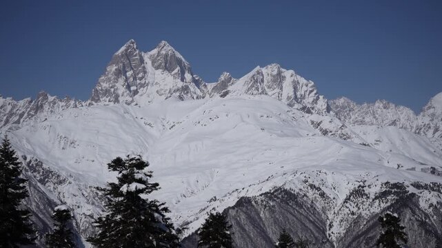 Handheld zoom toward Ushba peak in Caucasus Mountains, Georgia. Snowy forest foreground and dramatic alpine summit, natural camera shake creating real presence effect