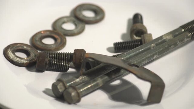 Close up of various rusty bolts, nuts, and washers rotating on a white surface. Industrial hardware components for repair, mechanical engineering, and construction concepts. High quality 4K macro foot
