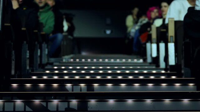 Audience watching performance from illuminated stairs and theater seating in dark venue