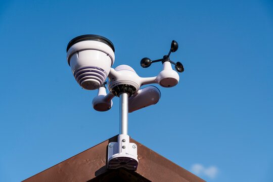 Weather station sensor installed on a rooftop against a clear blue sky, capturing data such as temperature, humidity, and wind speed for accurate forecasts and climate monitoring.