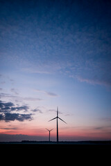 Obraz premium Two wind turbines against a blue and orange sky at sunrise, peaceful atmosphere, view across a misty field to two wind turbines during dawn, near 49424 Goldenstedt, Vechta district, Germany
