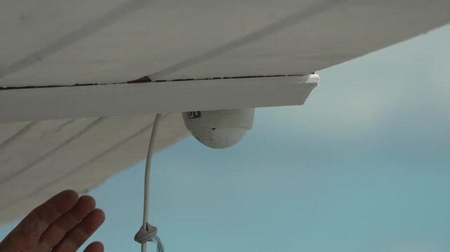 Security camera, installation, hand, man installing white dome security camera on house eaves against blue sky