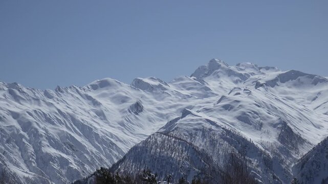 Handheld zoom shot of high snow-covered mountain peaks under clear sky. Slight camera shake adds a real immersive feeling of being in the mountains, natural travel atmosphere