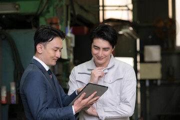 Obraz premium 工場でタブレットを見て相談する作業員と信金や銀行のビジネスマン、借り入れでdx活用現場のクローズアップ