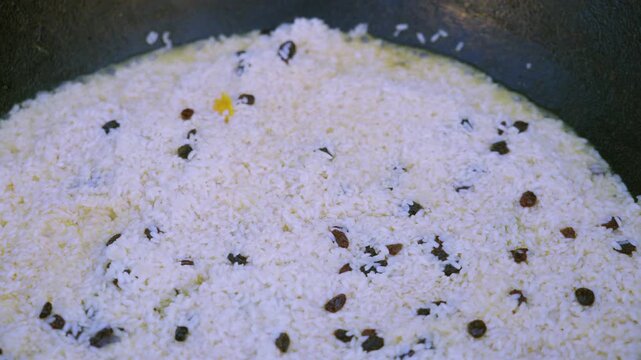 Young female cook tasting ready pilaf with spoon from large cauldron, close up
