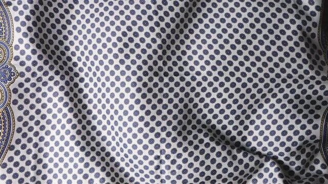 Silk fabric with abstract geometric print of small circles on white background waves in the wind. Natural silk texture creates soft folds and ripples forming an elegant background. 