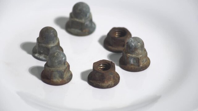 Macro 4K footage of rusty metallic acorn nuts or dome cap nuts rotating on a white background. These weathered fasteners highlight corrosion, industrial wear, and automotive aging, perfect for hardwar