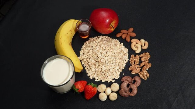 High angle of rotating organic oats with milk, fruits, and mixed nuts on black background, healthy meal mix.