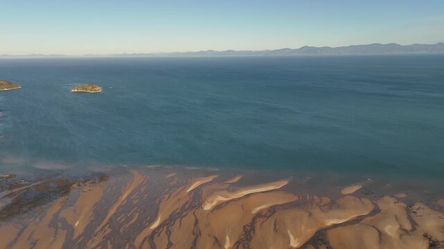 Panoramic drone view of Abel Tasman coastline near Marahau, New Zealand at sunset, revealing tidal sand patterns, calm ocean and small islands under warm golden hour light. Aerial top down.