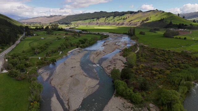 Aerial sunset view of Motueka River in Tasman region, South Island New Zealand, winding through green farmland and rolling hills with braided channels glowing in warm evening light. Flyover.