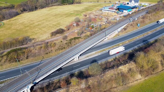 Aerial view of highway and railway bridge crossing rural farmland with truck traffic in Germany