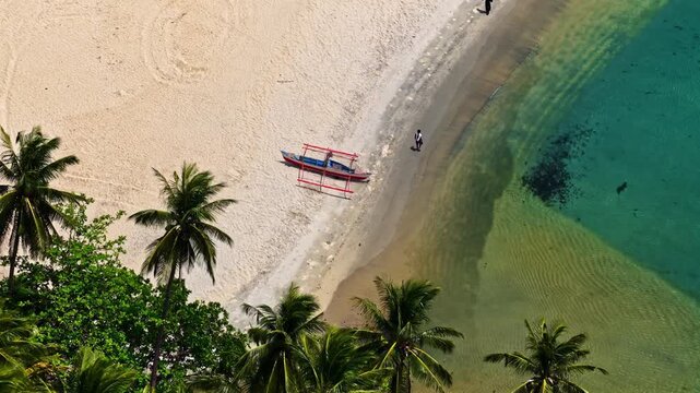 A traditional boat resting on a sandy beach lined with palm trees and clear turquoise water.