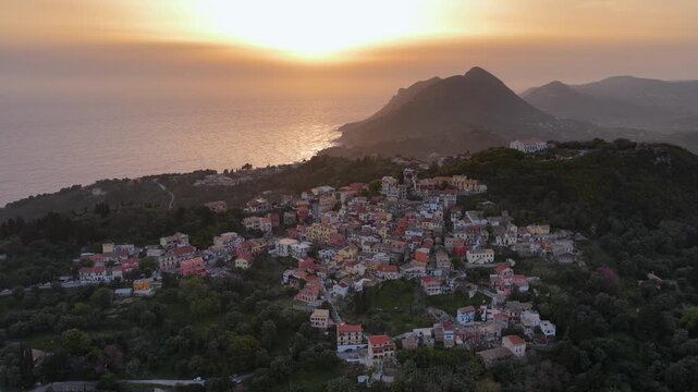 Aerial Sunset Over Pelekas Village in Corfu, Greece. Traditional Hillside Houses and Coastline Panorama at Golden Hour with Ionian Sea View