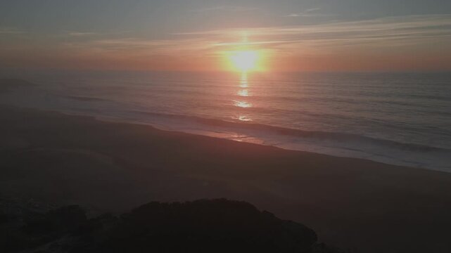 Aerial view of a romantic golden sunset over the Atlantic Ocean at Praia do Salgado in Nazare, Portugal. Calm waves wash onto the sandy shore during a peaceful summer evening on the coast