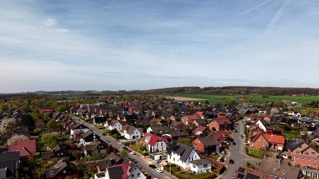 Aerial drone view of peaceful suburban neighborhood with single family homes and solar panels near open fields on a sunny spring day showing sustainable living and modern American suburb. Wide shot.