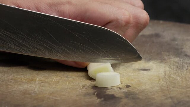 Close-up of chopping leek with knife on wooden board, focus on detail