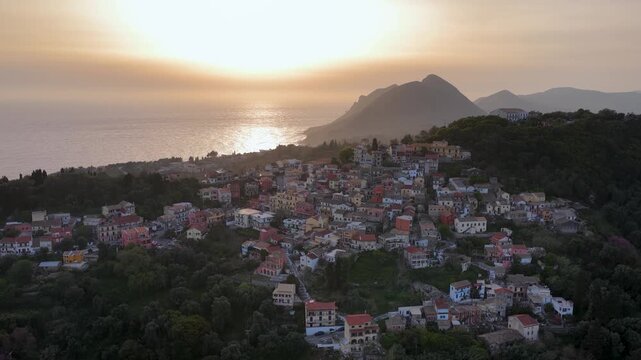 Aerial panoramic view of Pelekas village in Corfu Greece at sunset with golden sunlight over the Ionian Sea and lush green coastal mountains