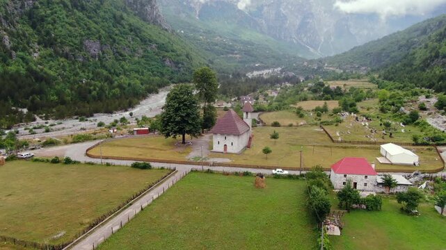 Stunning aerial footage showing the historic church of Theth, nestled in a lush green valley within the breathtaking Albanian Alps