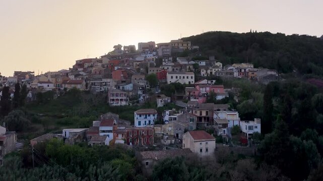 Scenic drone view of the picturesque hillside village of Pelekas in Corfu Greece during beautiful golden hour sunset with sun hiding behind the traditional buildings