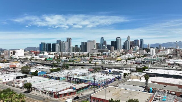 Cinematic aerial footage of Los Angeles, California showcasing the downtown skyline, colorful graffiti along freeway overpasses, and dense urban cityscape under clear skies.