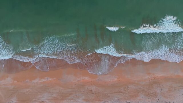 Cinematic top-down aerial drone footage of turquoise Atlantic waves crashing onto the golden sands of Saint Augustine Beach, Florida.