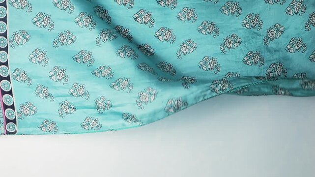 Natural silk fabric with blue floral pattern waving in the wind. Abstract background of turquoise textile creating soft flowing ripples and waves. Lightweight authentic silk material.
