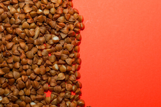 Premium buckwheat kernels densely fill the left side of the frame, creating a striking textured contrast with the smooth, vibrant orange background.