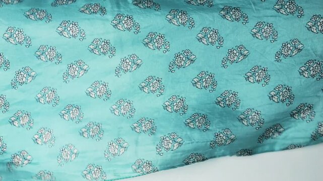 Natural silk fabric with blue floral pattern waving in the wind. Abstract background of turquoise textile creating soft flowing ripples and waves. Lightweight authentic silk material.