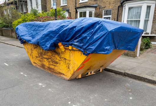 A residential construction waste skip with a blue cover on a suburban street.