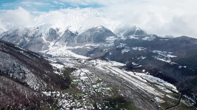 Aerial drone view of Mestia in Svaneti, Georgia with green valleys mixed with snow and high mountain peaks. Scenic landscape with traditional architecture, nature, travel, winter transition
