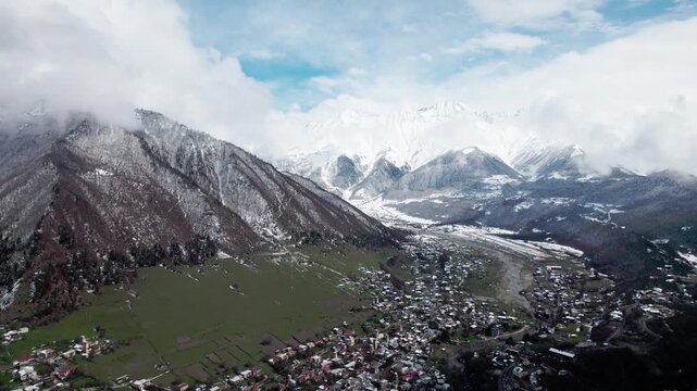 Aerial drone view of Mestia in Svaneti, Georgia with green valleys mixed with snow and high mountain peaks. Scenic landscape with traditional architecture, nature, travel, winter transition