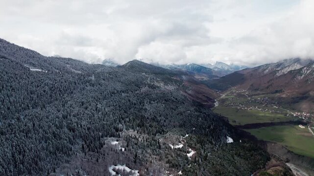 Drone flight over snowy pine forest and green valley in Svaneti, Georgia. Spring mountain landscape, contrast of snow and fresh grass, Caucasus mountains, scenic aerial nature view