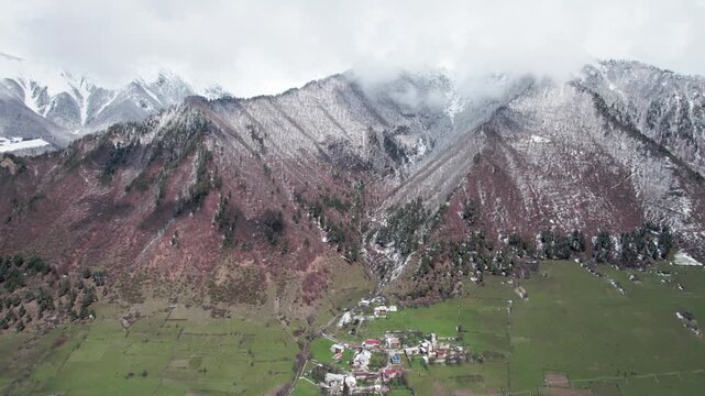 Aerial drone view of Mestia in Svaneti, Georgia with green valleys mixed with snow and high mountain peaks. Scenic landscape with traditional architecture, nature, travel, winter transition