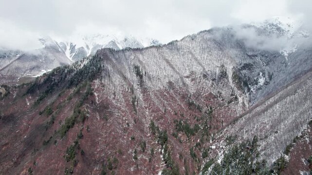 Drone view of Caucasus mountains with melting snow, early spring landscape, partially snow-covered slopes, clouds over peaks, natural seasonal change, scenic aerial nature