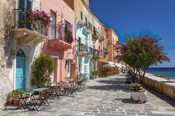 Obraz premium Historic Mediterranean town with pastel facades and lively street cafes along waterfront under clear blue sky, creating charming and vibrant coastal atmosphere