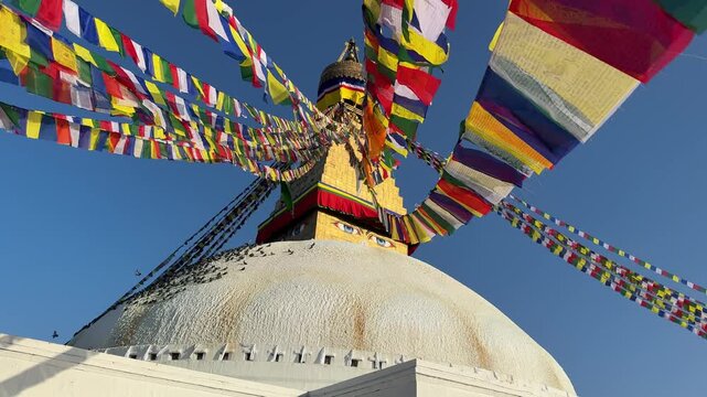 Slow motion pigeons flying around Boudhanath stupa in Kathmandu with colorful prayer flags waving in the wind. Spiritual atmosphere, Buddhism, travel, peaceful scene, cultural landmark