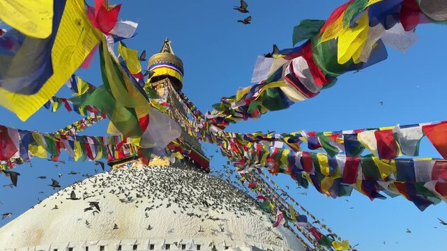 Slow motion pigeons flying around Boudhanath stupa in Kathmandu with colorful prayer flags waving in the wind. Spiritual atmosphere, Buddhism, travel, peaceful scene, cultural landmark