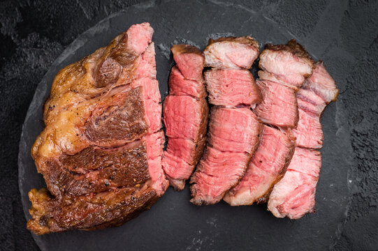 Sliced beef chuck eye roll steak cooked medium rare with juicy texture. Gourmet beef meat with salt on dark stone background.