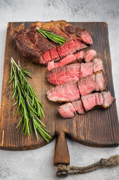 Juicy sliced beef chuck eye roll steak medium rare with rosemary on wooden board. Gourmet cooked beef food scene.
